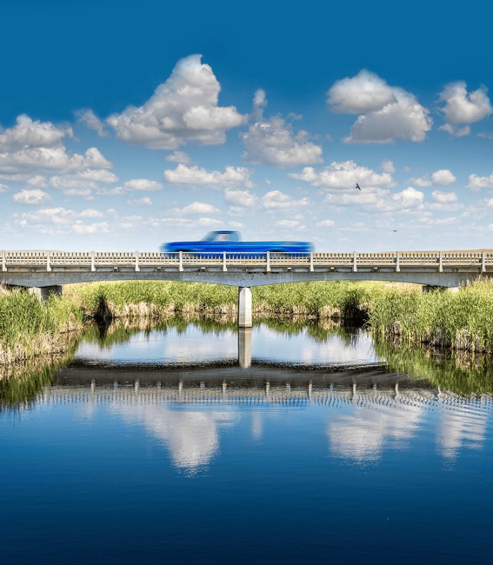 Blue pickup racing across a bridge overlooking a pristine blue river.